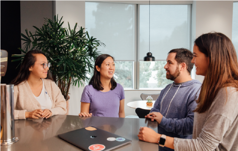 Three women and one man indoors, sitting around a table and talking (Summit Learning Platform, Annual Letter, CZI).