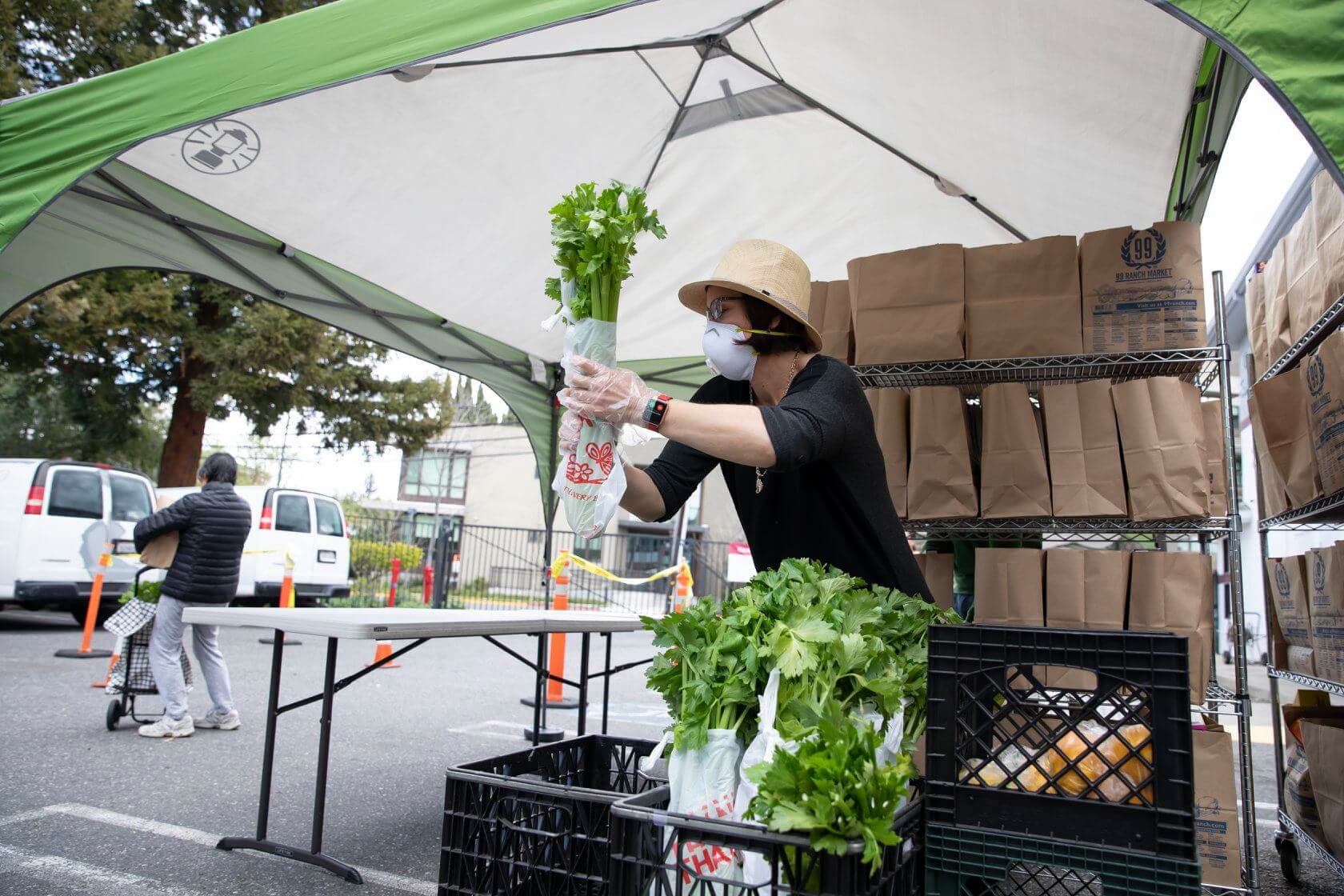 A masked woman under a canopy sorting groceries in a parking lot food distribution outlet (California Wildfire Relief and Resilience Efforts, Annual Letter, CZI).