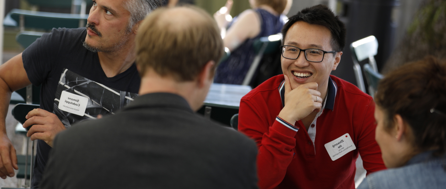 A diverse group of people sitting together, some individuals wearing glasses, discussing various topics in a casual setting.