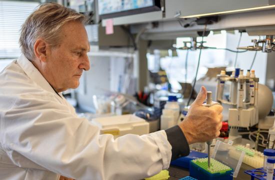 Chan Zuckerberg Biohub New York President Andrea Califano sits at a lab bench with his right arm outstretched and his hand holding a pipette.