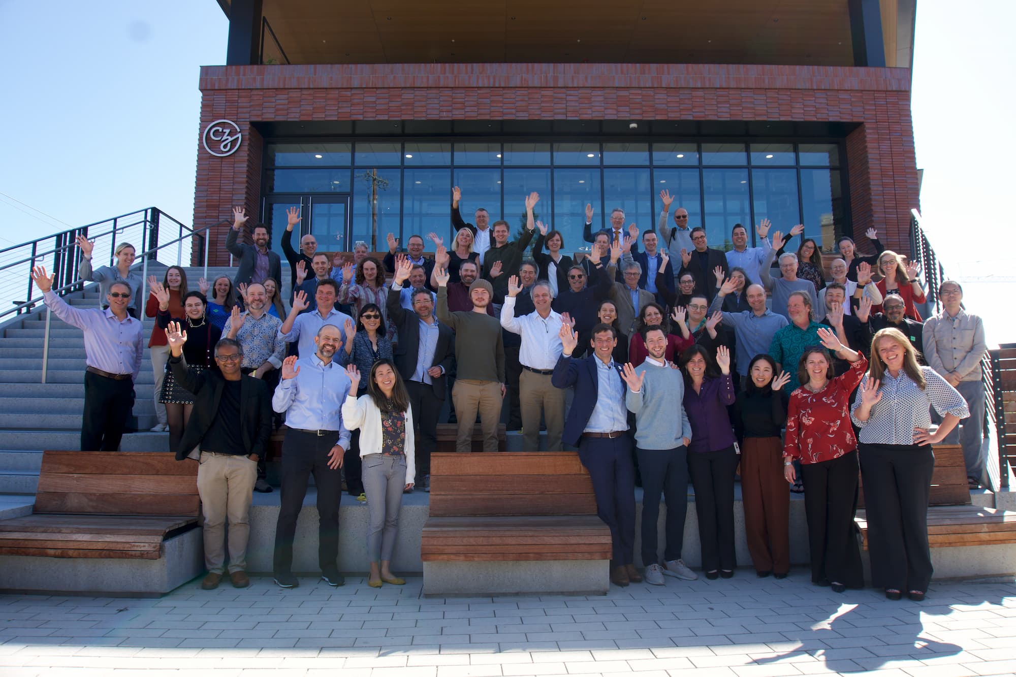 Participants of the Data-Driven Drug Repurposing Workshop stand outside CZI HQ on the stairs and smile and wave at the camera.