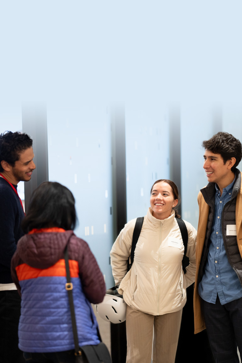 Four people stand in a small circle, smiling and talking with each other.