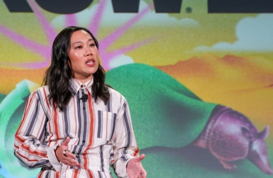 Priscilla Chan speaks on stage at SXSW, gesturing in a striped dress, with the SXSW logo and a colorful desert backdrop behind her.