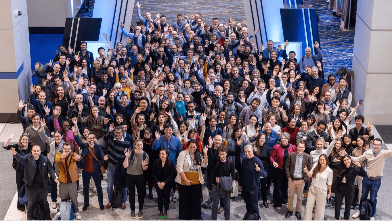 Participants of theCell Science 2025 Meeting stand and look up to the camera, waving and smiling.